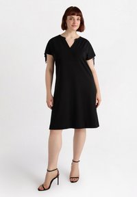 Czarna sukienka do kolan z dekoltem w serek i krótkimi rękawami. Wyposażona w sznurki na rękawach oraz gładki, lekki materiał. Zestawiona z czarnymi szpilkami.