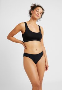 Svart bh- och bikinisett i mjukt, stretchigt tyg. Bhn har breda axelband och rundad urringning; bikinin har låg midja.