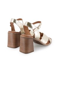 Sandalias de tacón cuadrado de cuero dorado con tiras anguladas y una hebilla, que cuentan con un tacón de madera texturizada y estriada y un diseño de punta descubierta.