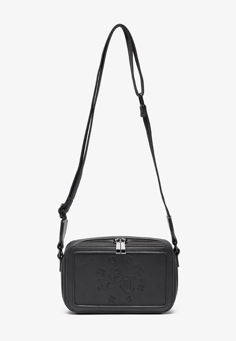 Black leather crossbody bag with a zip closure, embossed logo on the front, and adjustable strap. Smooth texture with a rectangular shape.