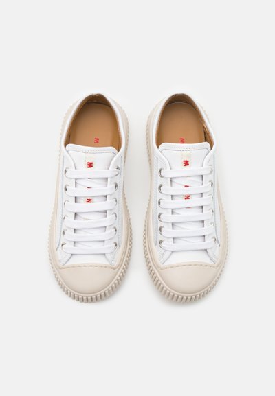 Sneakers bianchi con tomaia in pelle liscia, punta tonda, sei occhielli e suola in gomma beige con pareti laterali testurizzate. Dettagli di branding rossi.