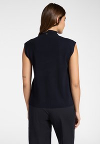 Top senza maniche navy con collo alto, caratterizzato da una texture liscia e un dettaglio brand sul retro. Abbinato a pantaloni scuri con stampa.