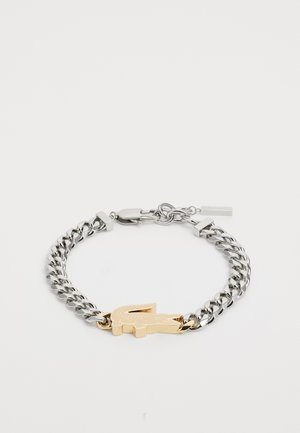 Silver chain bracelet featuring a gold-tone crocodile emblem, with linked design and clasp fastening. Smooth metal surfaces.