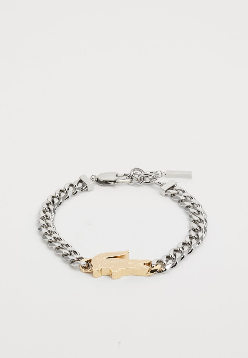Bracelet en chaîne argentée avec un emblème de crocodile doré, au design à maillons et fermeture à clip. Surfaces métalliques lisses.