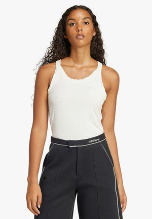 Top bianco senza maniche con scollatura arrotondata e bordi ondulati, abbinato a pantaloni neri a vita alta con piping bianco e dettagli con logo.