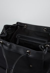 Black fabric bucket bag with leather accents, metal eyelets, drawstring closure, and an interior zippered pocket. Smooth texture throughout.