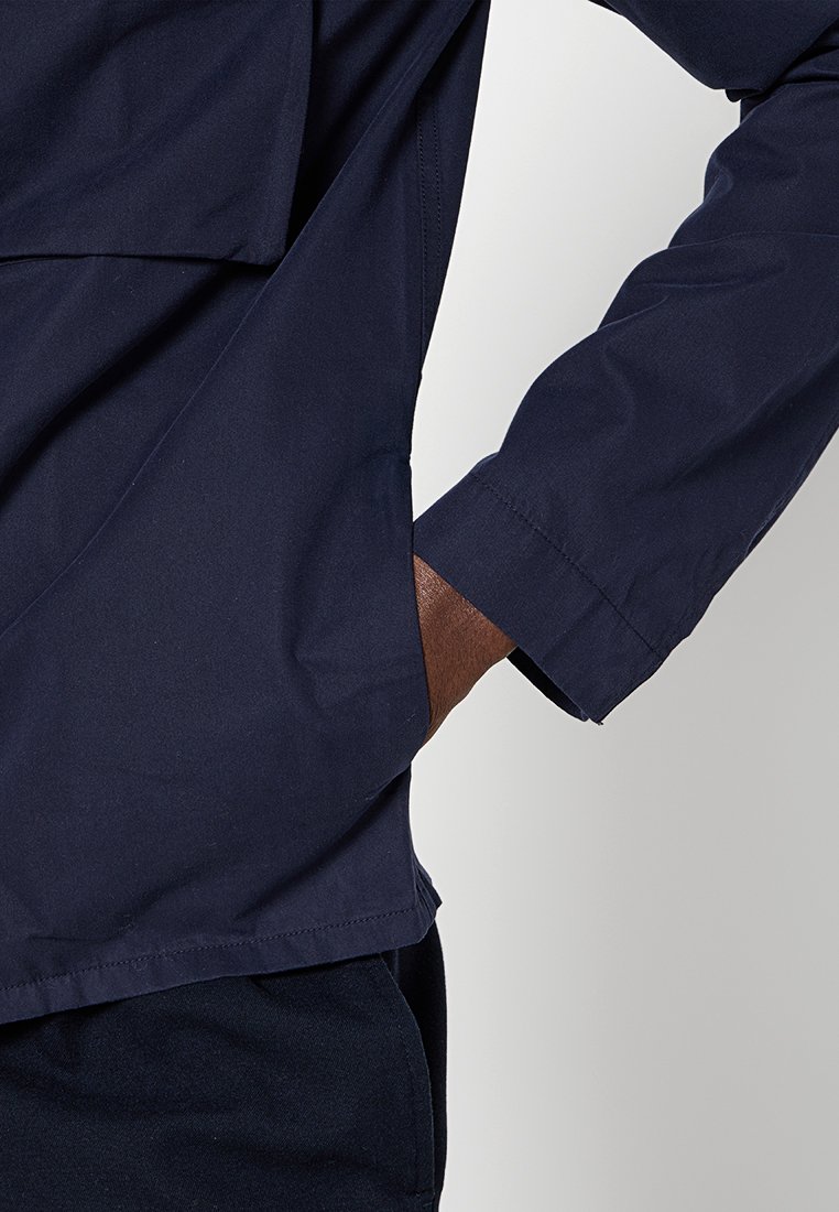 Camisa azul marino de corte relajado, con un bolsillo en el pecho y mangas largas. El material parece suave con una ligera textura mate.