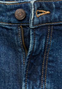 Nahaufnahme von Jeansstoff mit einem Metallknopf, messingfarbener Reißverschluss, orangefarbener Naht und einer leicht verblassten, tiefblauen Farbe mit glatter Textur.