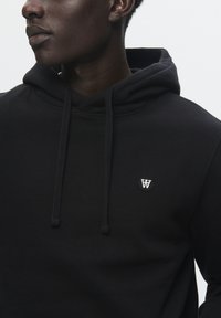 Black hoodie made of soft fabric, featuring a front pocket, drawstrings, and a small logo patch on the chest.