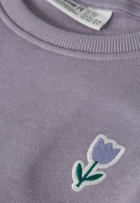 Liliowa bluza z wyszytym wzorem jasnofioletowego tulipana z zielonymi liśćmi. Miękka tekstura i detal z prążkowanym kołnierzem.