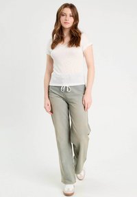 Haut blanc à manches courtes avec un col en V ; pantalon en denim vert ample avec taille à cordon ; texture douce ; associé avec des chaussures blanches.