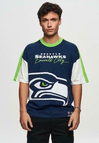 Blauw-witte T-shirt met korte mouwen en een groot Seattle Seahawks-logo, met groene accenten rond de kraag en mouwen, gemaakt van katoen.
