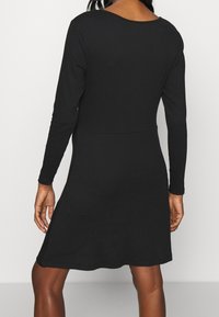 Svart långärmad klänning i stretchigt tyg, med rundad halsringning och utsvängd kjol. Slät yta utan synliga mönster.