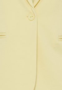 Blazer jaune clair avec un bouton unique à l'avant et deux poches fendues horizontales de chaque côté.