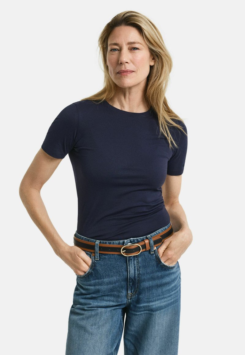 Marineblaues T-Shirt mit kurzen Ärmeln aus glattem Stoff, kombiniert mit hochtaillierten Denim-Jeans und einem braunen Gürtel mit einer runden Schnalle.