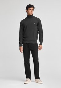 Maglione a collo alto grigio scuro realizzato in un tessuto a maglia testurizzato, abbinato a pantaloni neri e sneakers color crema. Presenta un piccolo logo sul petto.