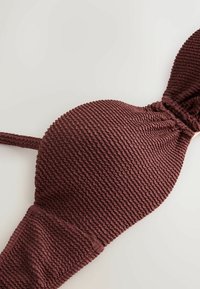 Barna, texturált anyagú bikini felső ráncolt mintával és állítható pántokkal, világos felületen laposan elhelyezve.