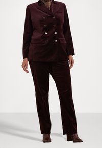 Burgundské sametové sako složené z dvojřadého blejzru se stříbrnými knoflíky a odpovídajícími kalhotami s rovnými nohavicemi. Texturovaný povrch.