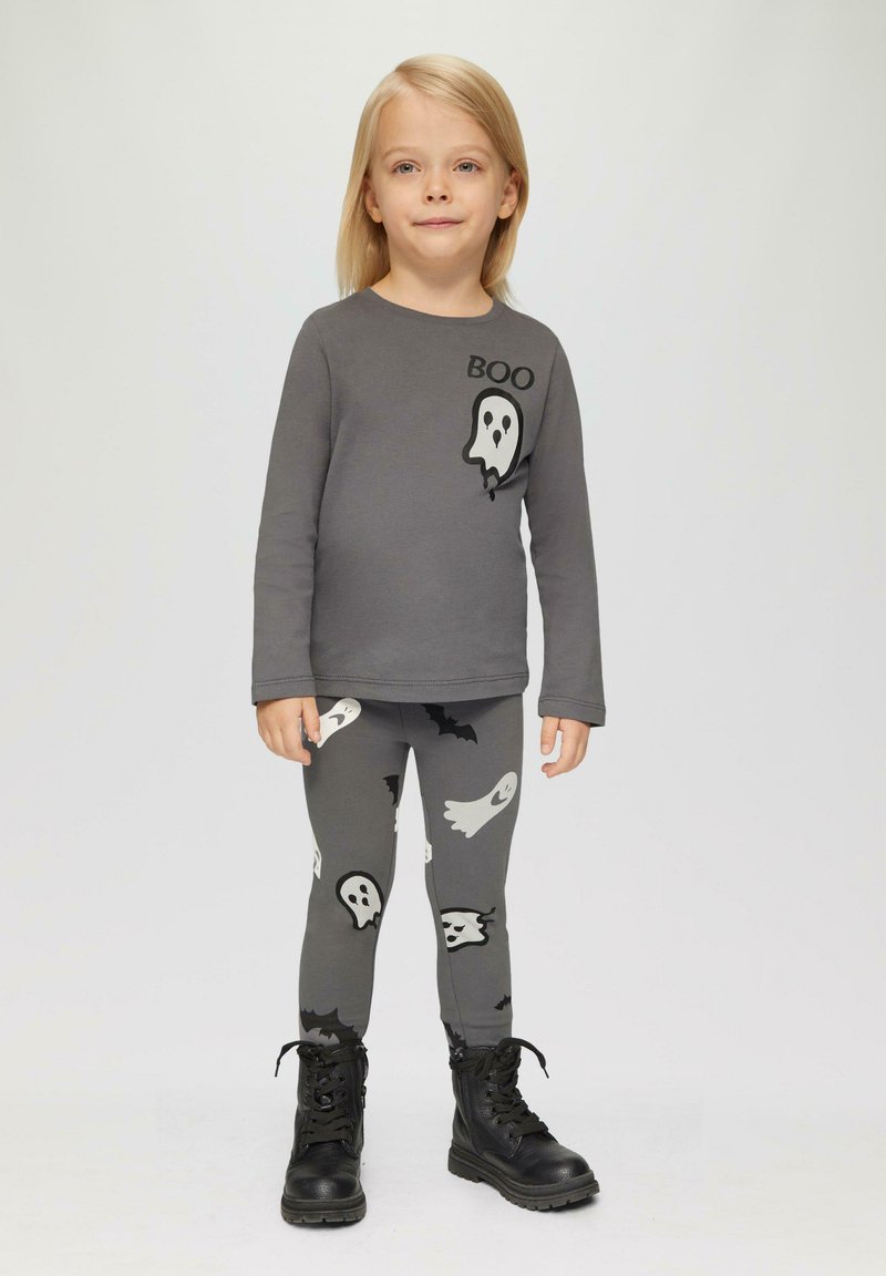 Graues Langarmshirt mit dem Text "Boo" und einem Gespenst-Graphic, kombiniert mit grauen Leggings mit Gespenster- und Fledermaus-Muster, getragen mit schwarzen Stiefeln.