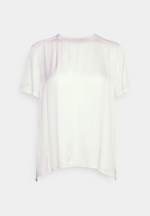 Blouse blanche en satin à manches courtes, col rond et légers fronces aux épaules, sur fond uni.