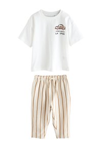 Chemise blanche à manches courtes avec un petit motif de voiture et le texte « Speed Series LA 1982 », associée à un pantalon beige avec des rayures verticales marron.