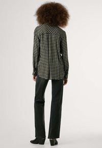 Blusa a quadri in bianco e nero con colletto, maniche lunghe e polsini con bottoni, abbinata a jeans svasati scuri e stivali neri con tacco.