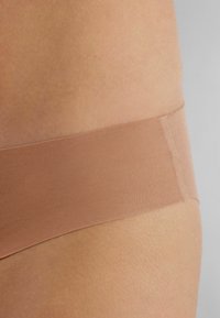 Naadloze beige ondergoed met een zachte, elastische tailleband. De stof heeft een gladde textuur, ontworpen voor comfort en minimale zichtbaarheid onder kleding.