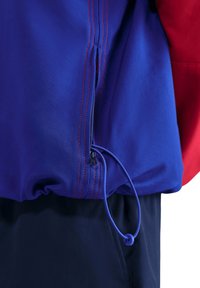 Kleurrijk jack met blauw materiaal en rode accenten, een ritssluiting en een trekkoord aan de zoom voor een verstelbare pasvorm.