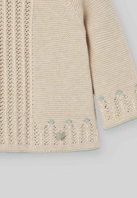Pullover beige lavorato a maglia con motivi testurizzati, caratterizzato da accenti azzurri e un dettaglio con bottone argentato sull'orlo. Tessuto morbido e traspirante.