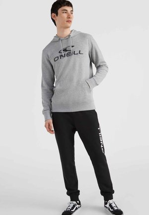 Grau Kapuzenpullover mit schwarzem O'Neill-Logo, schwarze Jogginghose mit weißem Branding und schwarze Schuhe. Der Stoff ist weich und strukturiert; körperbetonter Schnitt.