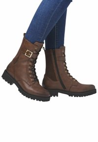 Botas de cuero marrón hasta el tobillo que presentan un diseño de cordones en la parte frontal, cremallera lateral, detalle de hebilla y suela de goma texturizada.