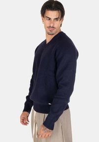 Maglione a costine di colore blu navy con scollo a V, maniche lunghe e vita aderente. Presenta un piccolo etichetta del marchio sul lato inferiore.