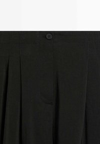 Schwarzer plissierter Rock mit Bund, Knopfverschluss und verdecktem Reißverschluss vorne.