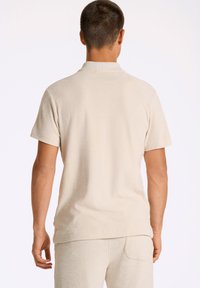 Beige frotté polo-shirt med avslappnad passform, korta ärmar och krage. Mjuk textur och minimalistisk design. Endast bakvy.