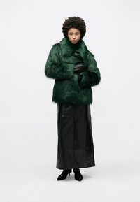Πράσινο παλτό από ψεύτικη γούνα με ψηλό γιακά και μακριά μανίκια, σε συνδυασμό με μαύρη δερμάτινη μακριά φούστα και μαύρες ψηλοτάκουνες γόβες. Ομαλή υφή, πλούσιο χρώμα.