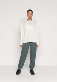 Light beige long-sleeve shirt with crew neckline, paired with dark teal tapered sweatpants and black athletic shoes.