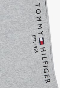 Šedé bavlněné tepláky s černě vyšitým textem "TOMMY HILFIGER" a "EST. 1985," s malým barevným blokovým logem.