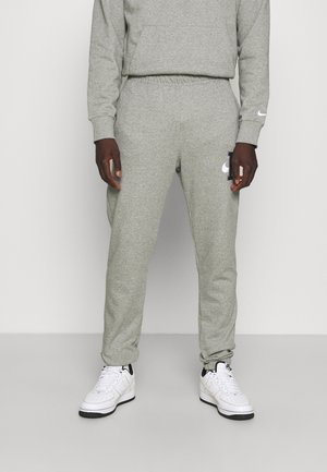 Osoba nosząca jasnoszare spodnie dresowe Nike i pasującą bluzę, połączone z białymi sneakersami Nike na jednolitym tle.