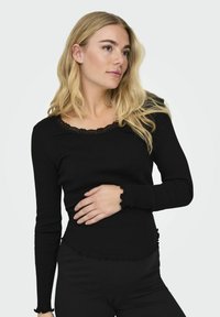 Must mustripi pika varrukatega topp, millel on laineline pitsist kaelus ja äär, millega koos on istuvad varrukad ja mugav siluett.