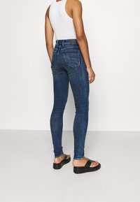 Jeans ajustados en denim azul oscuro con una cintura baja, que cuentan con bolsillos traseros y una silueta ajustada. Llevados con sandalias de plataforma negras.