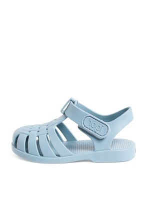 Light blue rubber sandal with a closed toe, open sides, adjustable strap, textured insole, and a logo detail on the side.