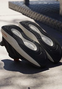 Zwei schwarz-weiße Sneakers, die verkehrt herum auf einer Gehwegoberfläche liegen, mit sichtbaren strukturierten Sohlen.