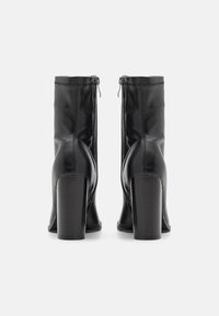 Bottines en cuir noir avec une texture lisse, talons carrés hauts et fermeture éclair à l'arrière. Les coutures ajoutent un intérêt visuel.