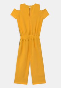 Macacão amarelo com mangas curtas abertas nos ombros, cintura elástica e pernas largas. Apresenta uma abertura em forma de olho de fechadura nas costas. Textura suave.