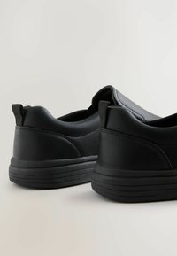 Black slip-on shoes featuring a smooth leather exterior, contoured side design, and textured rubber sole with vertical grooves.