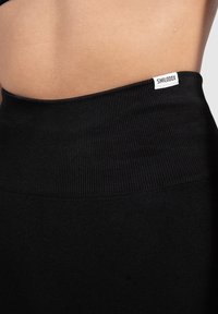 Czarne legginsy z wysokim stanem z prążkowanym pasem. Materiał wydaje się miękki i elastyczny, o gładkiej fakturze. Metka widoczna na pasie.