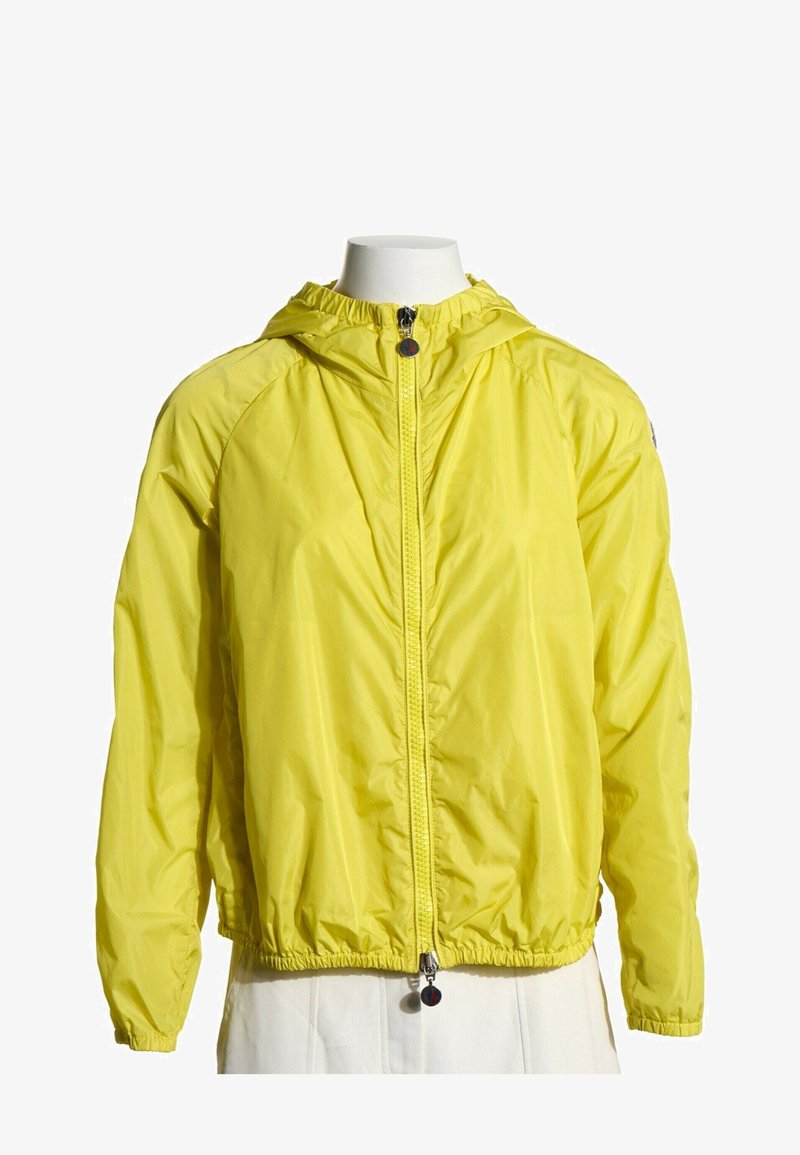 Veste légère jaune à capuche avec fermeture éclair frontale et poignets et ourlet élastiques, présentée sur un buste de mannequin blanc.