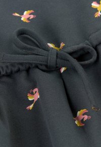 Tissu gris foncé avec un motif de petits flamants roses et jaunes, froncé à la taille avec une ceinture en tissu assortie.