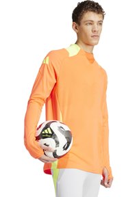 Langarm, felrood sportshirt met textuurpatroon en reflecterende accenten. Model houdt een zwart-wit voetbal vast.