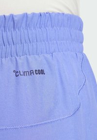Pantalones cortos deportivos de color púrpura claro con cinturilla elástica. Presenta el logo "CLIMACOOL" y detalles cosidos. Textura de tejido suave y lisa.